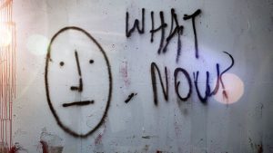 Image of graffiti on a wall that says "What Now?"